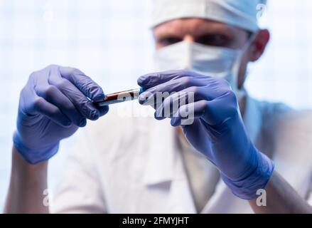 Hände eines Labortechnikers mit einem Röhrchen Blutprobe und einem Rack mit anderen Proben. Labortechniker hält die Blutprobe für die Studie Stockfoto