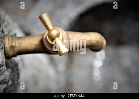 Blick von oben auf einen alten Wasserhahn. Der Messinghahn leuchtet hell in der Sonne. Fließendes Wasser sieht frisch aus. Die Tropfen haben ein schönes Bokey. Vintage. Rustikal. Stockfoto