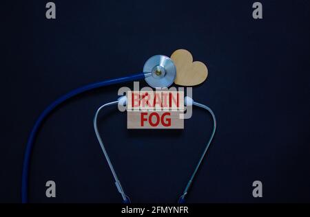 Medical, covid-19 und Gehirn Nebel Symbol. Holzblöcke mit den Worten „Hirnnebel“ und Stethoskop auf schwarzem Hintergrund. Holzherz. Medizinisch, covid-19 brai Stockfoto