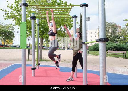 Zwei Freunde schwingen in einer Affenbar in einem Calisthenics Park und tragen Schutzmasken. Fitness im Freien. Stockfoto