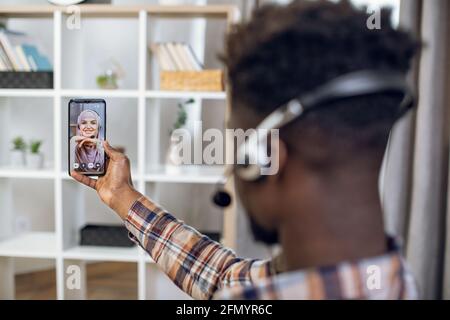 afroamerikanischer Mann im Headset mit modernem Smartphone für Videogespräche mit muslimischer Frau in Hijab. Junges Paar aus online während Pandemie. Stockfoto