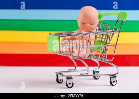 LGBT-Gemeinschaft und Kinder. Babypuppe in einem Warenkorb auf dem Hintergrund der LGBT-Flagge, das Konzept der Adoption, künstliche Befruchtung. Stockfoto