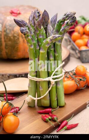 Isolierter frischer grüner Spargel auf altem Holztisch mit Tomaten und Ein Kürbis Stockfoto