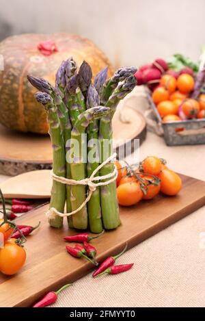 Isolierter frischer grüner Spargel auf altem Holztisch mit Tomaten und Ein Kürbis Stockfoto