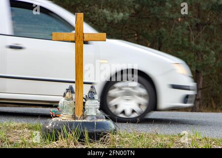 Ein Gedenkkreuz am Straßenrand mit Kerzen zum Gedenken an den tragischen Tod, auf einer Fahrt im Hintergrund verschwommenes Auto. Stockfoto