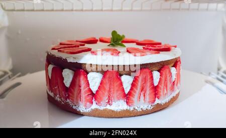 Erdbeer- und Sahnetorte mit frischem Minzblatt darauf In einem Kühlschrank Stockfoto