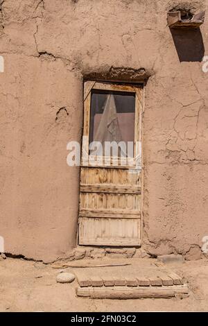 Rauh gehauene Holztür mit beschädigtem Schirm und hölzerner Veranda Im lehmziegelpueblo, das in Taos New Mexico wohnt Stockfoto