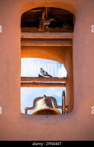 Vögel, die im Glockenturm der adobe-Missionskirche stehen Amerikanischer Südwesten mit blauem Himmel, der durchleuchtet - selektiver Fokus Nahaufnahme Stockfoto