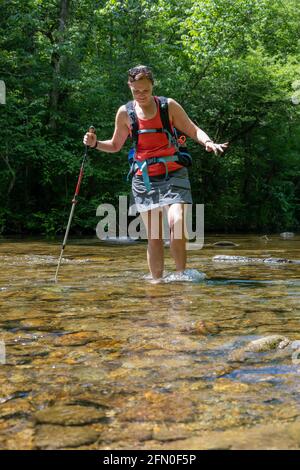 Frau kreuzt Stream in den Smokies mit Wanderstock für Gleichgewicht Stockfoto