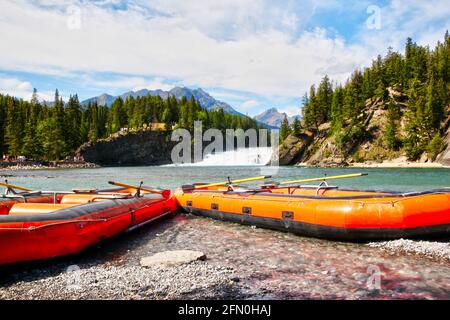 Rafting-Boote am Rande des Bow River mit Bow Falls und den Kanadischen Rockies of Banff National Park im Hintergrund. Stockfoto