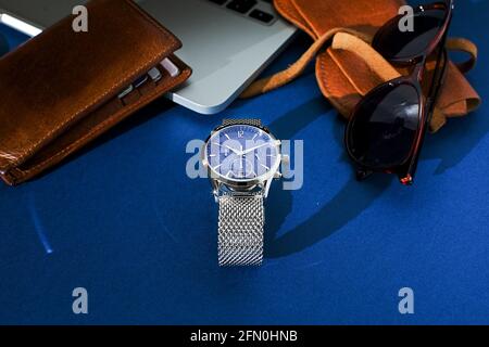 Ledertasche, Uhr mit Metallarmband, Sonnenbrille und Laptop auf blauem Hintergrund. Accessoires für Herren. Draufsicht Stockfoto