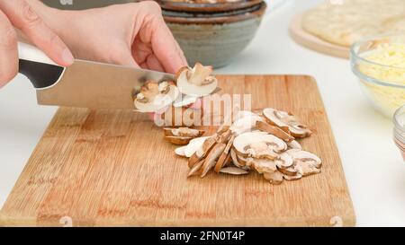 Frau schneidet Crimini Pilze auf Holz Schneidebrett. Schritt für Schritt Pilz Pizza Rezept Stockfoto