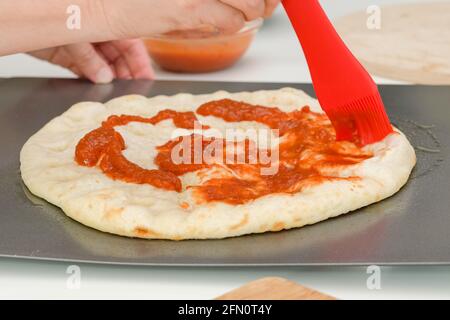 Pizzateig mit Tomatensauce bestreichen. Hausgemachte Mozzarella-Pilz-Pizza Schritt für Schritt Rezept Stockfoto