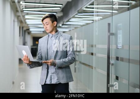 Glücklicher junger Mann, der im modernen Büro sitzt und sich anschaut Die Kamera mit einem Lächeln Stockfoto