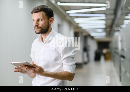 Porträt eines jungen Mannes in einem weißen Hemd im Büro. Der Manager im Büro hält einen Laptop in der Hand Stockfoto