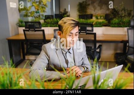 Ein junger asiatischer Manager arbeitet in einem Büro mit einem Laptop. Moderner Arbeitsplatz, Coworking Stockfoto