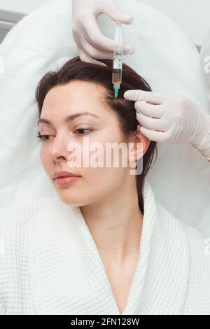 Eine Frau bekommt einen Schuss in den Kopf in einer Kosmetologie-Klinik. Mesotherapie für das Haarwachstum. Stockfoto