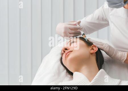 Eine Frau bekommt einen Schuss in den Kopf in einer Kosmetologie-Klinik. Mesotherapie für das Haarwachstum. Stockfoto