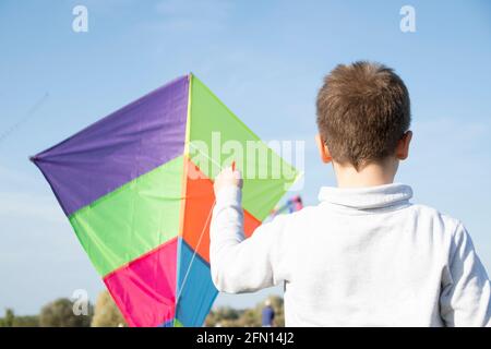 Ein Junge spielt und beobachtet fliegende Drachen am blauen Himmel. Stockfoto