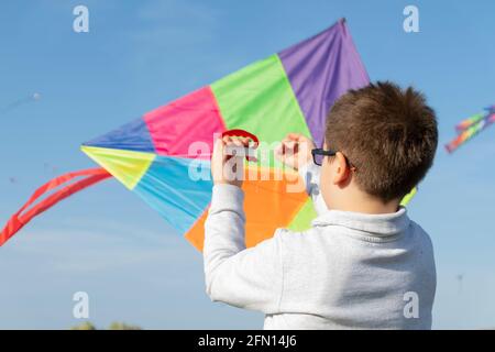 Ein Junge spielt und beobachtet fliegende Drachen am blauen Himmel. Stockfoto