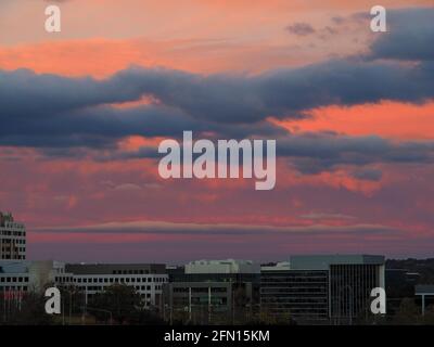 Sonnenuntergang, Reihen von rosa, blau-grauen und weißen Wolken über leuchtend rosa und orange Himmel, während der Sonnenuntergang auf die östliche Canberra Skyline reflektiert, Gebäude Stockfoto