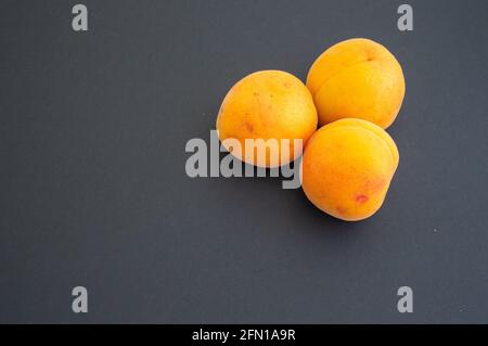 Drei Aprikosen in einem Haufen auf der Seite. Platz für Text auf grauem Hintergrund Stockfoto