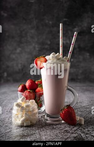 Ein kaltes Getränk. Milchiger Erdbeermilchshake, mit frischen Erdbeeren und Rahm. In einem hohen transparenten Glas, einem dezenter, dunkler Moor. Kopierraum Stockfoto