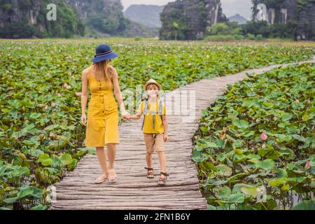 Mutter und Sohn in Gelb auf dem Weg zwischen dem Lotussee. Mua Cave, Ninh Binh, Vietnam. Vietnam wird nach der Quarantäne Coronovirus COVID 19 wieder geöffnet Stockfoto