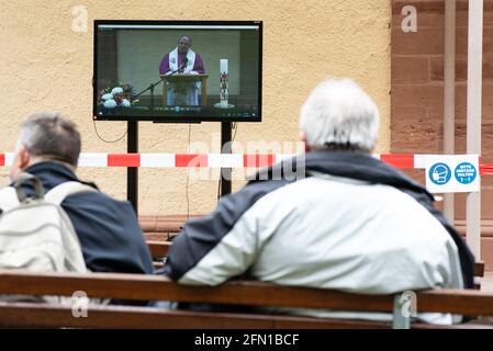 Wachstedt, Deutschland. Mai 2021. Gläubige sitzen während der alternativen Männerwallfahrt unter dem Motto "Komm Herr, segne uns" vor der Wallfahrtskirche Klüschen Hagis und schauen auf ein Fernsehgerät mit einer Aufnahme von Bischof Ulrich Neymeyr. Himmelfahrt ist der Tag der Männerwallfahrt nach Klüschen Hagis in der Diözese Erfurt. Wie im vergangenen Jahr wird die traditionelle Wallfahrt wegen Corona abgesagt. Quelle: Swen Pförtner/dpa/Alamy Live News Stockfoto