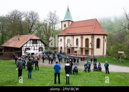 Wachstedt, Deutschland. Mai 2021. Gläubige stehen während der alternativen Männerwallfahrt unter dem Motto 'Komm Herr, segne uns' vor der Wallfahrtskirche Klüschen Hagis und schauen auf ein Fernsehen mit einer Aufnahme des Bischofs. Himmelfahrt ist der Tag der Männerwallfahrt nach Klüschen Hagis in der Diözese Erfurt. Wie im vergangenen Jahr wird die traditionelle Wallfahrt wegen Corona abgesagt. Quelle: Swen Pförtner/dpa/Alamy Live News Stockfoto