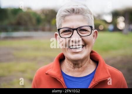 Glückliche ältere Frau, die im Stadtpark vor der Kamera lächelt - Fokus auf Gesicht Stockfoto
