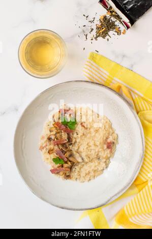 Risotto mit Pilzen, grünem Tee und italienischem Speck. Weißer Hintergrund und gelbes Handtuch Stockfoto