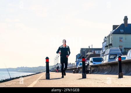 Blick auf die Küste von Herne Bay mit drei Pollern im Vordergrund und einem Mann, der gegen den klaren weißen Himmel auf den Betrachter zuläuft. Stockfoto