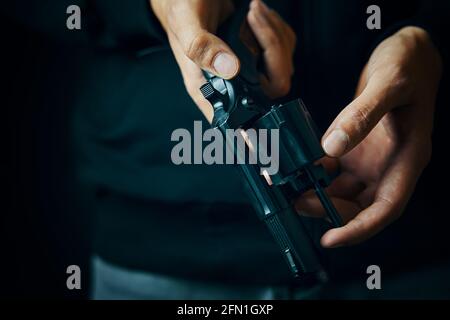 Herrenhände prüfen im Revolverfass auf Kugeln. Nahaufnahme der Person, die die Waffe nachlädt. Guy bereitet Pistole für Schüsse vor. Schusswaffe zur Verteidigung oder zum Angriff. Stockfoto