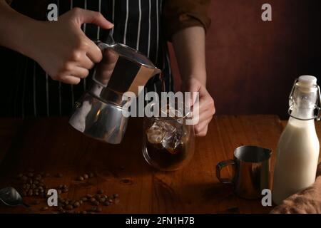 Ein kurzer Schuss Barista, der Kaffee mit Eis in die Tasse gießt An der Theke aus Holz im Café Stockfoto