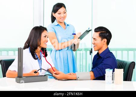 Asiatische Frau Doktor Check-up Blut Druck auf Patienten, während Krankenschwester schreiben auf Zwischenablage Stockfoto