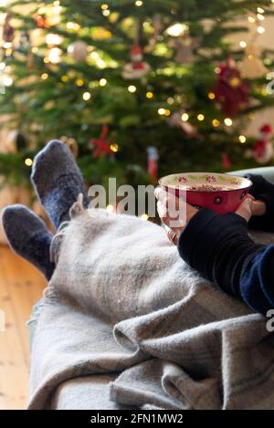 Eine große Tasse heiße Schokolade wird vor einem Weihnachtsbaum gehalten - wohlig. Stockfoto