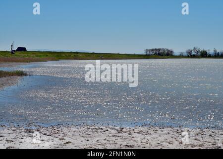 Österreich, Landschafts- und Rastplatz mit altem Ziehbrunnen und Strohjurte in der Nähe eines kleinen Steppensees, wo das Sonnenlicht in den Wellen im Neusiedle bricht Stockfoto