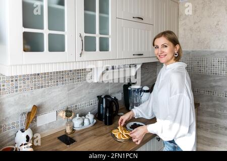 Eine Erwachsene Frau steht in der Küche und hält Pfannkuchen. Stockfoto
