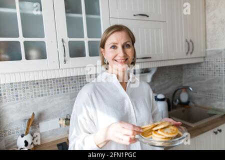 Eine Erwachsene Frau steht in der Küche und hält Pfannkuchen in den Händen. Stockfoto