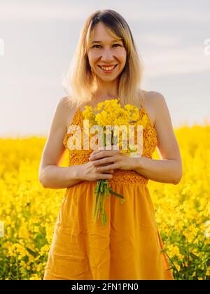 Porträt einer lächelnden Frau auf blühendem Rapsfeld mit Abendlicht. Gelbe Blumen und glückliche Frau Stockfoto
