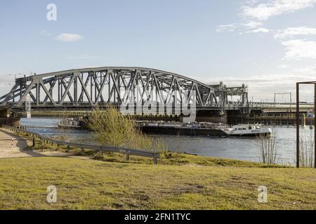 ZUTPHEN, NIEDERLANDE - 20. Apr 2021: Stahlzug und Verkehr ziehen eine Brücke über die IJssel mit einem Frachtschiff, das in der Nähe der niederländischen Hanse vorbeifährt Stockfoto