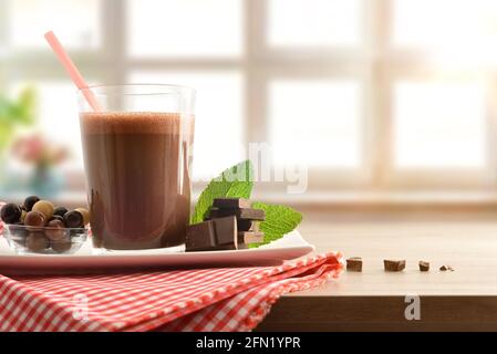 Glas mit Milchschokolade schütteln auf Servierteller mit Schüssel Voller Schokoladenkugeln und Portionen auf rot und weiß Karierte Tischdecke auf einem Tisch mit l Stockfoto