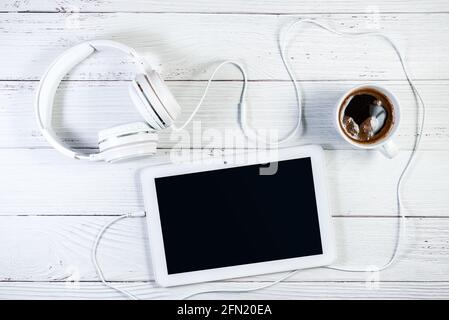 Weißes Tablet mit Kopfhörern und Kaffee auf weißer Holzoberfläche. Musik-Tablet-Modell. Beschneidungspfad für Bildschirmkopierbereich Stockfoto