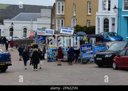 Seefischerstände konkurrieren um Kunden unter den Urlaubern, die zum hübschen Hafen in Tenby schlendern. Stockfoto