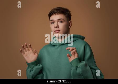 Junger verängstigte Mann im Sweatshirt auf braunem Hintergrund. Stockfoto