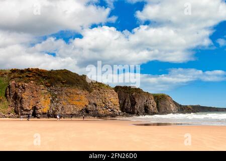 LUNAN BAY UND STRAND ANGUS SCHOTTLAND MENSCHEN IM SÜDEN ENDE DES SANDSTRANDES UND KLIPPEN MIT ZWEI HÖHLEN Stockfoto