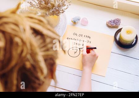 Draufsicht des Mädchens Berechnung der Lebenswegnummer auf dem Papier in der Starttabelle. Spirituelle Numerologie Konzept. Stockfoto