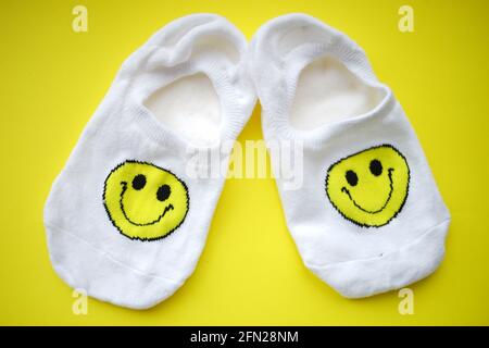 Zwei weiße Socken mit einem Smiley-Gesicht auf einem gelben Tisch. Stockfoto