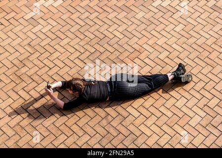 Eine junge Frau, die während des Laying Down ein Foto macht, Brighton Seafront, Brighton, East Sussex, Großbritannien. Stockfoto